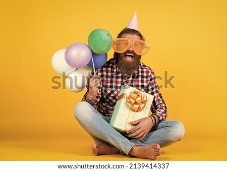 happy handsome bearded guy with unshaven face and stylish hairdo wear casual clothes holding present and party balloons, business reward