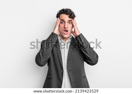 young businessman looking unpleasantly shocked, scared or worried, mouth wide open and covering both ears with hands