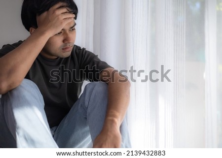 Young man with depression sitting alone in bed room. Depressed man must stay in home quarantine due to covid-19. sad depression female. unhappy, failure, sadness concepts. Royalty-Free Stock Photo #2139432883