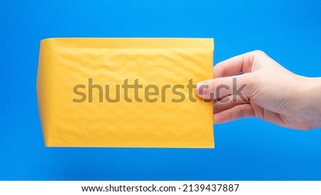 Yellow Bubble Mailer In Hand On A Blue Background