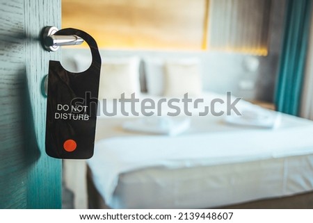 "Do not disturb" wooden plate sign which is hanging on the door handle. Close-up at the object, selective focus at partial part of the text. Sign on the door do not disturb in hotel