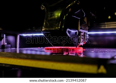 Automatic three dimensional printer machine printing red flat plastic model at modern technology exhibition - close up. 3D printing, futuristic, prototype, manufacturing and production concept Royalty-Free Stock Photo #2139452087