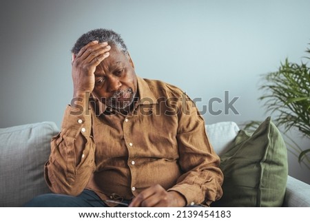 An adult has a headache. He sits and holds his hands on his head in a dark room. Concept of dramatic loneliness, sadness, depression, sad emotions, disappointment, nursing, pain. Royalty-Free Stock Photo #2139454183