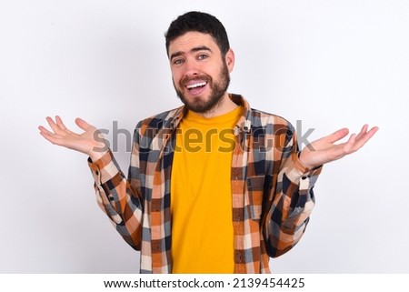 So what? Portrait of arrogant young caucasian man wearing plaid shirt over white background shrugging hands sideways smiling gasping indifferent, telling something obvious. Royalty-Free Stock Photo #2139454425