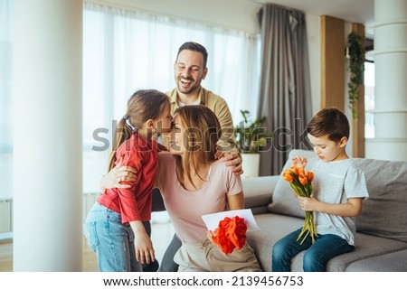 Happy mother getting gifts from kids at home. Mother´s Day - two children surprise their mother at home. Happy young family of four celebrating mothers day