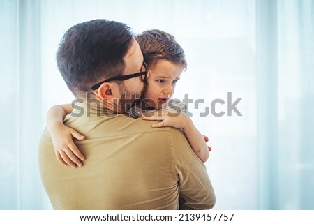 Father comforting stressed sad son. Close up of  father consoling his small sad son at home. Small boy crying in his father's hug at home.