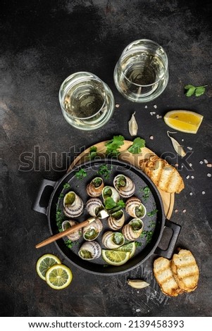Snails baked with sauce, Bourgogne Escargot Snails and wine glass. Baked snails with butter and spice. gourmet food. vertical image. top view. place for text. Royalty-Free Stock Photo #2139458393