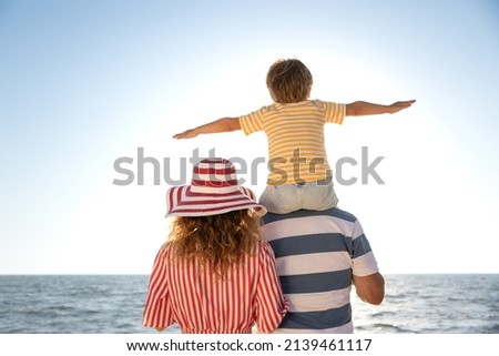 Happy family having fun on the beach. Mother, father and child against blue sea and sky background. Summer vacation concept. Rear view portrait