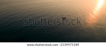 Drone aerial of fishing boat sailing in the sea to catch fish at sunset.