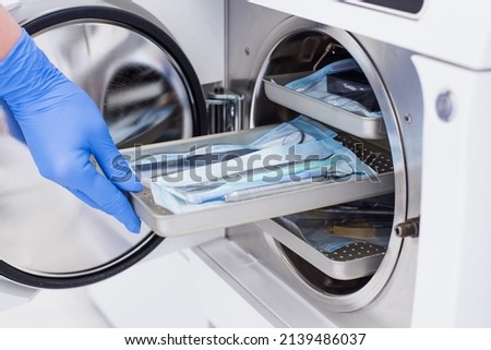 Assistant's hand in gloves insert packaged dental instrument to the autoclave to sterilise. Royalty-Free Stock Photo #2139486037