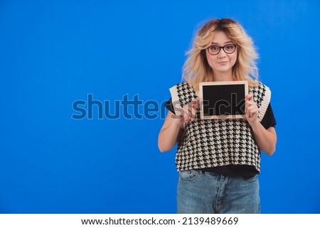 Beautiful caucasian woman wearing glasses and holding tablet or blackboard to camera. Copy space. Isolated. Blue background. . High quality photo