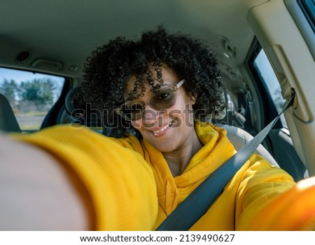 Close-up of Smiling young Latin American woman taking selfie picture in car.
