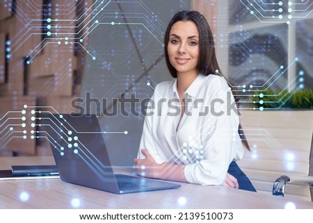 Attractive businesswoman in white shirt at workplace working with laptop to optimize development by implying new technologies in business process. Hi tech hologram over office background