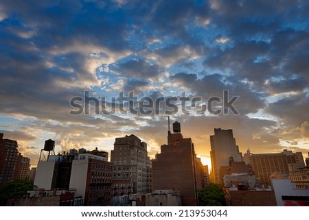 Blue hour over Manhattan, New York, and its skyline dotted with water tanks. The sunset enhances the clouds in the evening light and gives off a warm orange glow on Chelsea buildings.