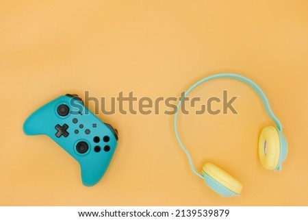 Green joystick gaming controller with green wireless headphone isolated on pastel yellow background, Video game console developed Interactive Entertainment Royalty-Free Stock Photo #2139539879
