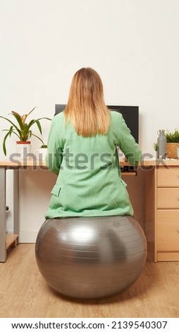Unrecognizable woman working from home uses fitness ball as a chair wears photo from behind