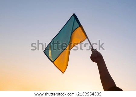 flag of ukraine in hand against the background of a yellow-blue sunset sky.