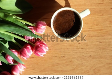 Cup of coffee and bouquet on wooden table. Morning light
