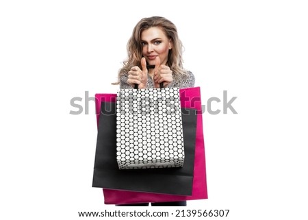 Smiling woman with paper shopping bags. Beautiful blonde woman in a leopard print shirt holds her thumbs up. Isolated on a white background.