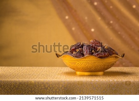 A golden bowl filled with fine quality Arabian dates. A studio shot of sacred date fruits against golden background with clear space for text. Royalty-Free Stock Photo #2139571515