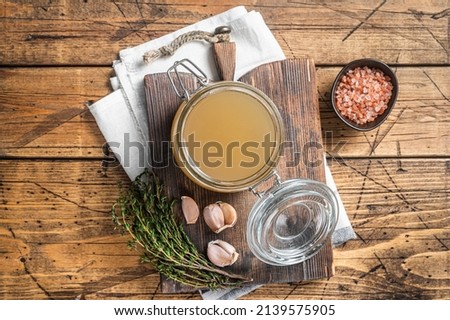Bone broth for chicken soup in a glass jar. Wooden background. Top view.