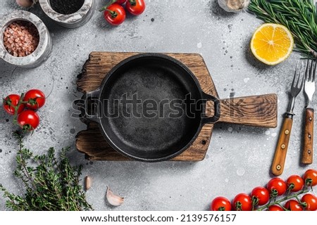 Various organic spices, herbs and ingredients around empty aged cooking skillet. Gray background. Top view. Copy space.