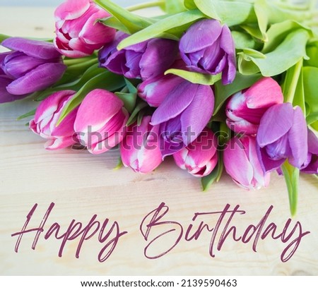 pink and violet tulips on wooden ground with happy birthday text background