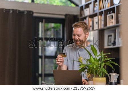 Picture of delighted adult man, looking at his credit card and smiling.