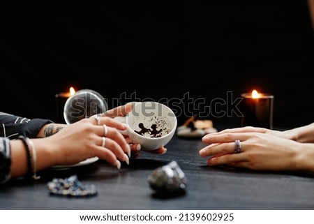Side view close up of female fortune teller reading coffee grounds telling destiny in seance with young woman in dark Royalty-Free Stock Photo #2139602925