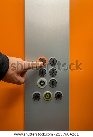 Man's hand pressing the button to go up to the third floor of an elevator. Close shot of an orange elevator and a finger pressing the button that makes the elevator go up to his floor.