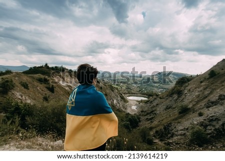 woman with dark hair wrapped in the flag of Ukraine on a background of mountain landscape