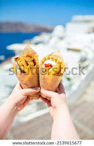Greek gyros wrapped in pita bread photographed against traditional greek town with white houses Royalty-Free Stock Photo #2139615677