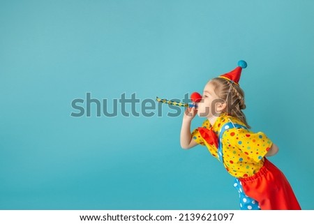 Funny kid clown against blue background. Happy child playing with festive decor. Birthday and 1 April Fool's day concept. Royalty-Free Stock Photo #2139621097