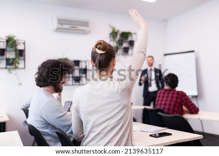 Students listening to a lecturer in a classroom. Smart young woman rasing hand during class. Royalty-Free Stock Photo #2139635117