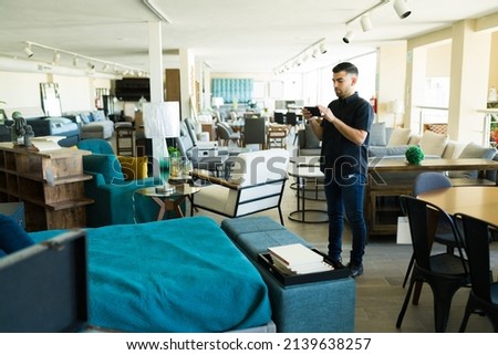 Handsome man taking pictures of the beautiful furniture and texting at the store while shopping for new decoration