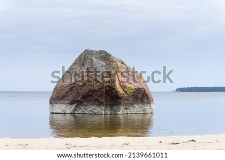 One single rock ib low water. Glacial erratic boulder on Kaberneeme beach (Kolga Bay, Finnish Gulf,  Baltic Sea, Estonia). Rohusi island in the background. Calm sea water, blue scene. Royalty-Free Stock Photo #2139661011