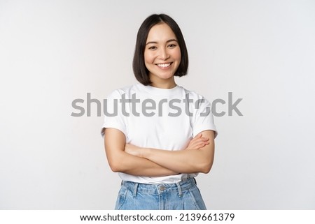 Portrait of happy asian woman smiling, posing confident, cross arms on chest, standing against studio background