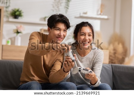 Asian young couple sitting on couch in living room enjoy playing video games spending time together. Happy couple play video games at home both are smiling, laughing and enjoying moment on weekend. Royalty-Free Stock Photo #2139669921