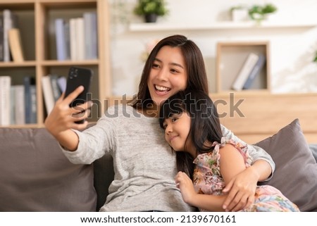 Asian mom and her kid are calling on smartphone. Both happy using cellphone for video call smiling mom and girl having fun greetings online with making video call communication through application. Royalty-Free Stock Photo #2139670161