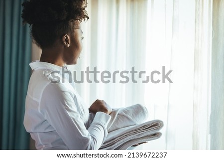 Female chambermaid holding clean white folded towels in bedroom. Young hotel maid putting stack of fresh white bath towels on the bed sheet. Cleaning the hotel room. 