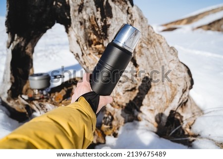 Thermos for tea, hold in your hands a thermos with a hot drink, camping utensils, black thermo bottle. High quality photo