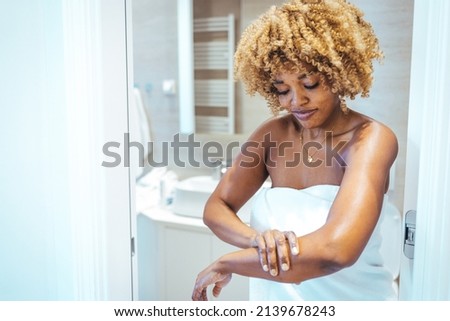 Concept of beauty procedure. Cropped view of afro american woman in bathrobe spending morning in bathroom, applying cream on soft skin. Taking care of yourself 