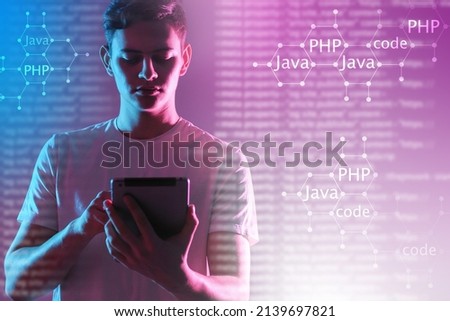 Programming languages, coding. Young programmer with a tablet against the background of programming languages. Machine code languages on a neon technological background. Programming concept. 