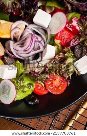 Fresh greek salad with tomato, radish, onion, bel pepper , olives and feta cheese on black plate, closeup view, wooden background.