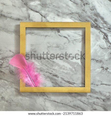 One pink feather in a gold frame. Gray white marble background. Text space. Top view. Minimal style.