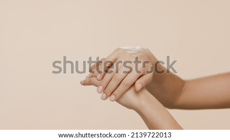 Horizontal close-up shot of female hands are rubbed and interlocked on beige background | Dry hands prevention concept Royalty-Free Stock Photo #2139722013