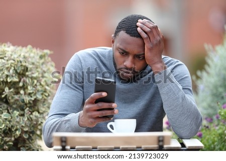 Front view portrait of a worried man with black skin checking phone in a coffee shop Royalty-Free Stock Photo #2139723029