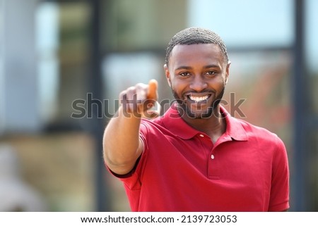 Front view portrait of a happy man with black skin pointing at camera in the street