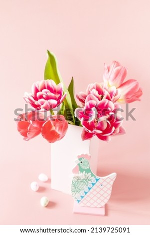 Bouquet of pink and purple tulips with colorful quail eggs over pink background. Spring and Easter holiday concept. 