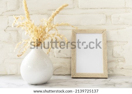 White picture frame mockup. White wall background. Scandinavian interior, neutral color palette with dry grass. Selective focus. 